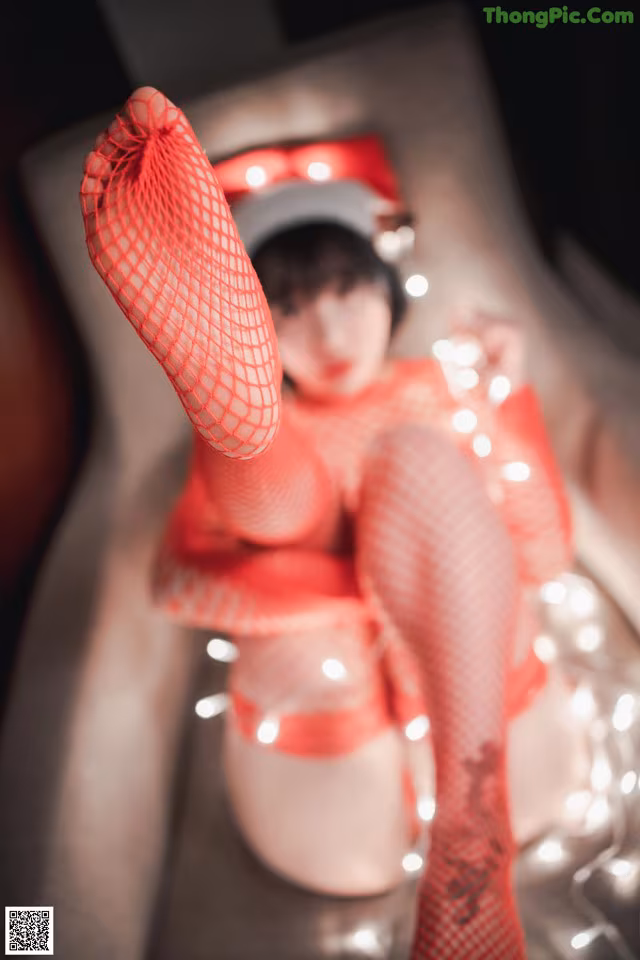 A woman in a red dress and fishnet stockings sitting on a bed.