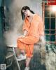 A woman sitting on a ladder in an orange jumpsuit.