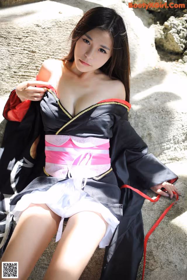 A woman in a black and pink dress sitting on a rock.