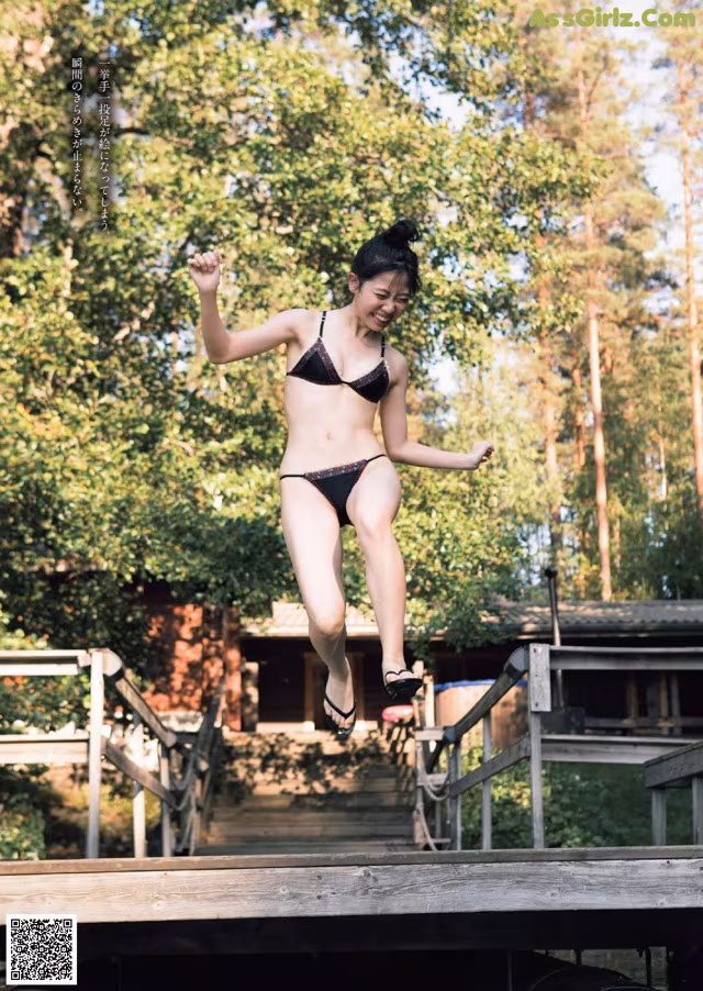 A woman in a bikini jumping off a wooden bridge.