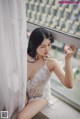 A woman in a white lingerie sitting by a window.