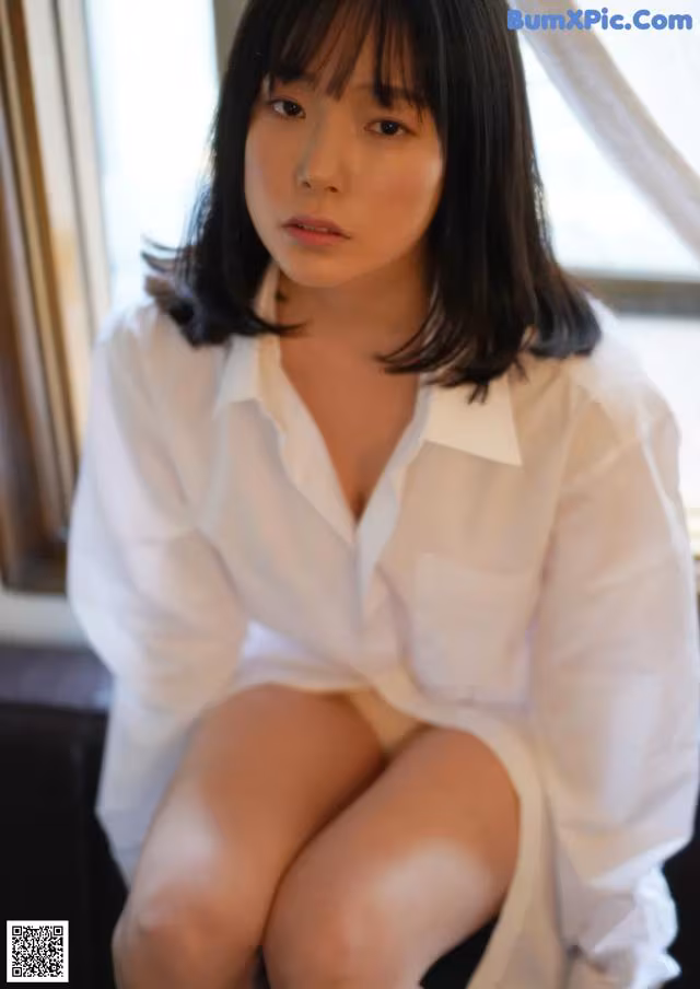A woman in a white shirt sitting on a window sill.
