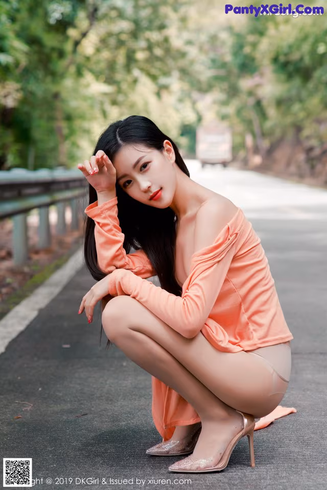 A woman in an orange dress crouching down on the road.