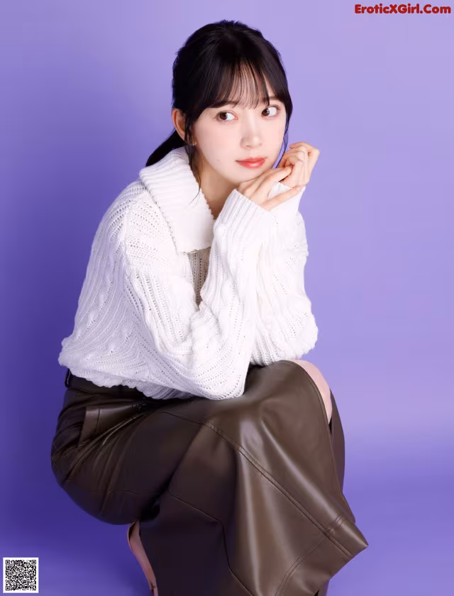 A woman in a white sweater and brown skirt posing for a picture.