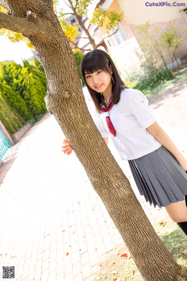 A woman in a school uniform leaning against a tree.