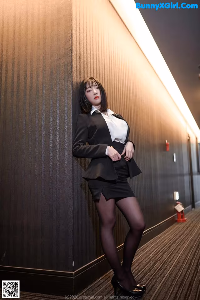 A woman in a business suit leaning against a wall.