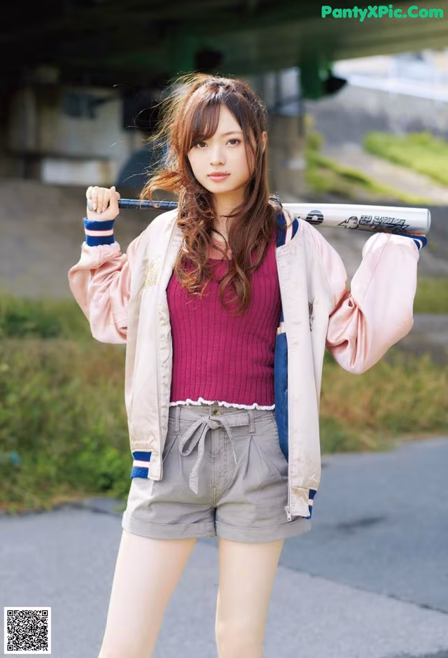 A young woman holding a baseball bat on a street.