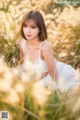 A woman in a white dress sitting in a field of tall grass.