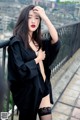 A woman in a black shirt and stockings posing on a balcony.