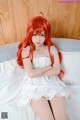 A woman with long red hair sitting on a bed.